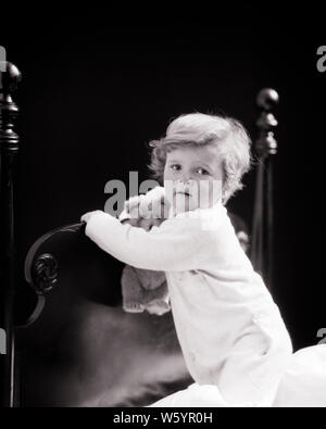 1920er Jahre 1930er Jahre bedtime Junge Kleinkind mit TEDDYBÄR HOLDING am Kopfteil des Bettes TRAGEN VON DR. DENTON SCHLAFANZUG MIT KAMERA-j 4976 HAR 001 HARS B&W AUGENKONTAKT TEDDYBÄR KOPFTEIL ZU KONZEPTIONELLEN STILVOLLE BABY BLANKET SLEEPERS GENERICIZED TRADEMARK JUNGEN SCHWARZEN UND WEISSEN KAUKASISCHEN ETHNIE GEHEN ZU SCHLAFEN HAR 001 ALTMODISCH Stockfoto