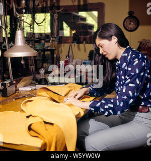 1970 lächelnde Frau HANDWERK HANDWERKLICHE ARBEITEN MIT LEDERWAREN AUF ARBEITSTISCH HOLDING KLEBSTOFFE SCHEREN TRANSISTOR RADIO LICHT-ks 11887 HAR 001 HARS JOBS KOPIEREN RAUM MIT HALBER LÄNGE DAMEN HANDWERK PERSONEN INSPIRATION ARTIST BERUF HANDWERK VERTRAUEN FREIHEIT SKILL BERUF GLÜCK Fähigkeiten gut gelaunt waren TRANSISTOR KARRIERE WISSEN STOLZ AUF BERUFE LÄCHELT SMALL BUSINESS KUNST FREUDE STILVOLLE TRANSISTOR RADIO KREATIVITÄT PRÄZISION ENTSPANNUNG WORKSHOP junger Erwachsener KUNSTHANDWERKERIN KAUKASISCHEN ETHNIE HAR 001 ALTMODISCH Stockfoto