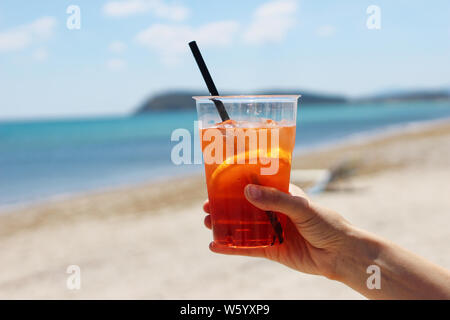 Nahaufnahme des womans Hand gekühlt aperol Cocktail mit Orange Slice, Trinkhalm und Eiswürfel, Italienisch alkoholische Getränk. Unscharfer Hintergrund wit Stockfoto