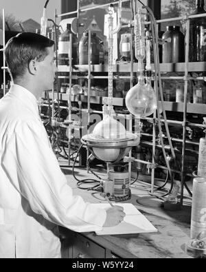 1950er Jahre 1960er Jahre junge Forscher DIE DURCHFÜHRUNG VON EXPERIMENT IN DER CHEMIE LABOR UNTER GLAS BECHER UND FLASCHEN - s12030 HAR 001 HARS MÖGLICHKEIT LEITENDE BERUFE HÖHERE BILDUNG HOCHSCHULEN KONZEPTIONELLE KREATIVITÄT PRÄZISION junger erwachsener Mann inmitten von SCHWARZEN UND WEISSEN KAUKASISCHEN ETHNIE HAR 001 ALTMODISCH Stockfoto