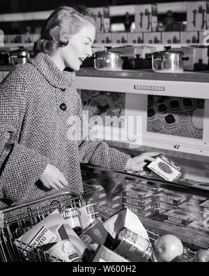 Frau SENGENDEN MANTEL SHOPPING IN TIEFKÜHLKOST IM SUPERMARKT - s 5920 HAR 001 HARS HAUSWIRTSCHAFTSLEITERIN KÄUFER GLÜCK HAUSFRAUEN FRÖHLICHE HOHEN WINKEL KART WARENKORB KARREN HAUSFRAUEN LÄCHELT FRÖHLICH stilvolle Mitte - Mitte - ERWACHSENE FRAU SCHWARZ UND WEISS KAUKASISCHEN ETHNIE HAR 001 ALTMODISCH ABSCHNITT Stockfoto