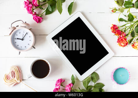 Tablet, Wecker, Tasse Kaffee, Rosen, Kerzen auf dem Tisch. Frauen Dinge Mode Frauen Schreibtisch Draufsicht Mockup Flach Kopieren Raum Stockfoto