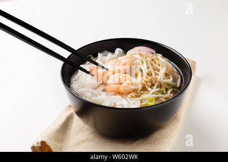 Traditionelle vietnamesische Nudelsuppe pho mit Garnelen in schwarz Schüssel auf weißem Hintergrund Stockfoto