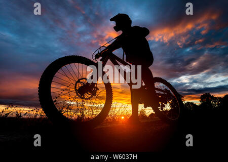 Downhill Mountainbike rider Silhouette bei Sonnenuntergang mit Full Face Helm Stockfoto