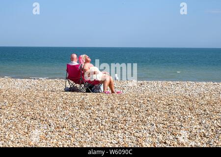 Ältere Paare sitzen auf Stühlen beim Sonnenbaden auf einer leeren Bognor Regis Strand mit dem Meer im Hintergrund, West Sussex England Großbritannien Stockfoto