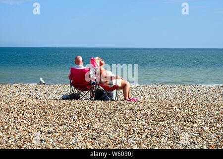 Ältere Paare sitzen auf Stühlen beim Sonnenbaden auf einer leeren Bognor Regis Strand mit dem Meer im Hintergrund, West Sussex England Großbritannien Stockfoto