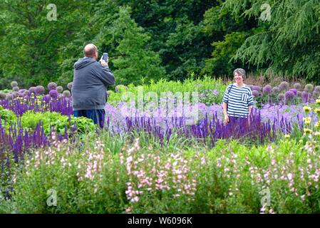 Touristen, die sich in der Royal Botanical Gardens, Kew, Fotos von sich selbst gegen die bunten Blumenrabatten, West London England Großbritannien Stockfoto