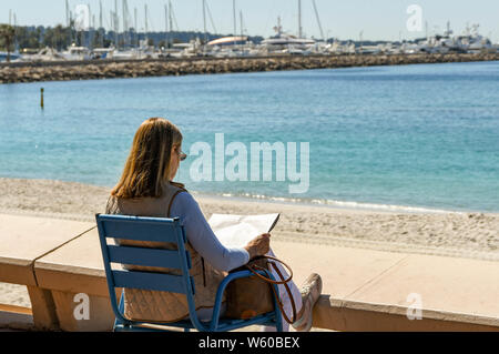 CANNES, Frankreich - April 2019: Person sitzen beim Lesen einer Zeitung auf der Promenade in Cannes an der Französischen Riviera. Stockfoto