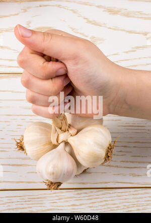 Hand, die Knoblauchzehen auf einer hölzernen Textur Stockfoto