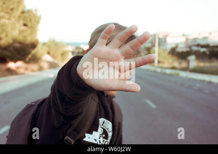 Jugendlicher verbirgt sein Gesicht mit Palmen auf Asphalt Stockfoto