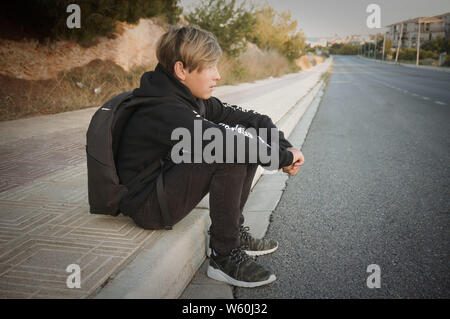 Blonde Teenager sitzen auf Asphalt Asphalt tragen schwarze Kleidung und Rucksack Stockfoto