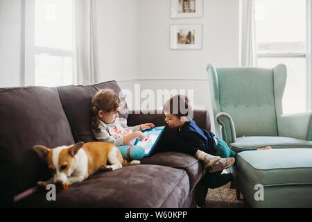 Jungen und Mädchen sitzen auf der Couch mit corgi pupply und Tablet Stockfoto