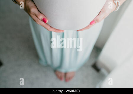 Bauch und Händen der schwangeren Frau, die im Hintergrund unscharf Füße Stockfoto