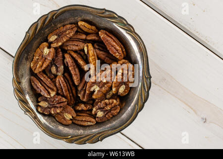 Menge ganze Frische braune Pekannuss Hälfte in Altes Eisen Schüssel flatlay auf weißem Holz Stockfoto