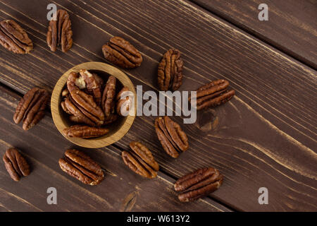 Menge ganze Frische braune Pekannuss Hälfte in eine hölzerne Schüssel flatlay auf braunem Holz Stockfoto