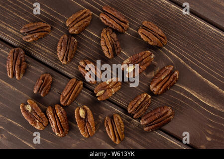 Menge ganze Frische braune Pekannuss Hälfte flatlay auf braunem Holz Stockfoto