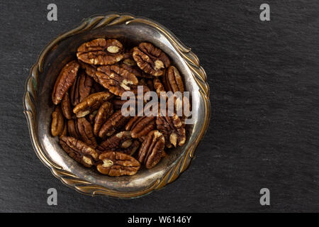 Menge ganze Frische braune Pekannuss Hälfte in Altes Eisen Schüssel flatlay am grauen Stein Stockfoto