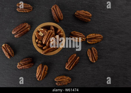 Menge ganze Frische braune Pekannuss Hälfte in eine hölzerne Schüssel flatlay am grauen Stein Stockfoto