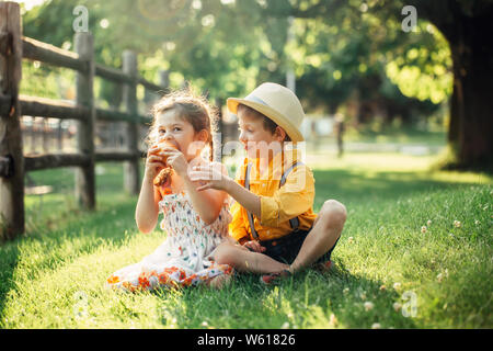 Kaukasische Kinder Jungen und Mädchen Geschwister zusammen sitzen, die gemeinsame Nutzung von Apple. Zwei Kinder Bruder und Schwester Essen süße Frucht im Park im Sommer Tag. Beste fr Stockfoto