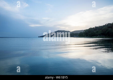 Krokodil geformte Berg entlang des Sees mit blauen Reflexionen bei Sonnenuntergang bei El Remate, Guatemala Stockfoto