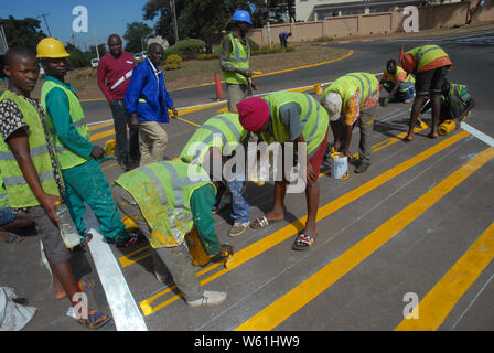 Die Beschäftigten im Straßenverkehr Malerarbeiten Zebrastreifen Streifen auf der Fahrbahn, Lilongwe, Malawi, Afrika. Stockfoto