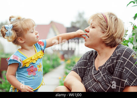 Enkelin Großmutter feeds Beeren in der Gegend Stockfoto