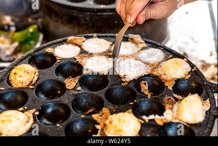 Mörtel - geröstete Gebäck oder "Kanom Krok' ist für traditionelle thailändische Dessert. Frau Hand entfernen Kanom Krok von Herd durch die Löffel. Street Food in Thailand. Thai Stockfoto