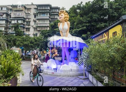 Eine Frau, die Zyklen der Vergangenheit eine riesige Statue des späten amerikanischen Schauspielerin Marilyn Monroe vor einem Einkaufszentrum in Chengdu City, im Südwesten Chinas Sichuan pro Stockfoto