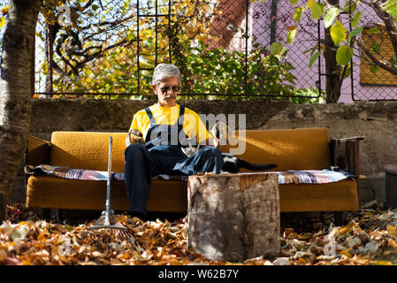 Mann auf dem Sofa sitzen nach der Reinigung Laub im Hof Stockfoto