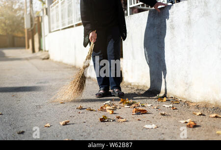 Ältere Frau Reinigung gefallenen Blätter im Herbst auf der Straße Stockfoto
