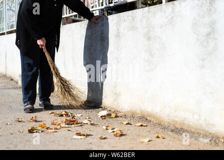 Ältere Frau Reinigung gefallenen Blätter im Herbst auf der Straße Stockfoto