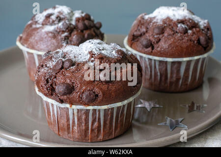 Drei chocolate Muffins liegen auf einem Schild vor dem Hintergrund einer türkisfarbenen Tisch. Feier. Geburtstag. Weihnachten und neues Jahr. Stockfoto