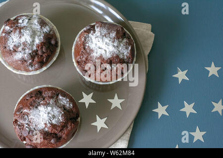 Drei chocolate Muffins liegen auf einem Schild vor dem Hintergrund einer türkisfarbenen Tisch. Feier. Geburtstag. Weihnachten und neues Jahr. Stockfoto