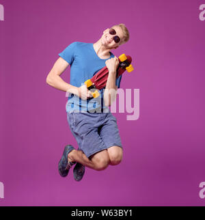 Mann mit Skate Board in der Hand auf lila Hintergrund, Penny wenig Board, Bewegung Stockfoto