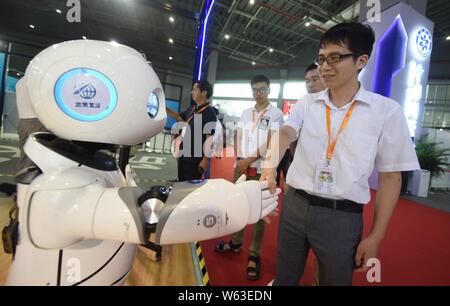 Ein chinesischer Besucher schüttelt Hände mit einem intelligenten Roboter auf dem Display während der 20. China International Industry Fair (CIIF 2018) in Shanghai, China, Stockfoto