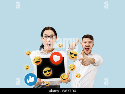 Social media Interaktionen auf Handy. Internet digital Marketing, Chatten, Kommentieren, Sympathie. Lächeln und Symbole über Tablet Bildschirm, der eine Beteiligung von jungen Paar auf Blau studio Hintergrund. Stockfoto