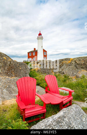 Zwei leere Adirondack Stühle vor dem Hintergrund der Fisgard Leuchtturm. Stockfoto