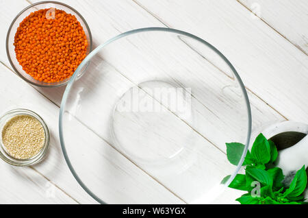 Glasplatten mit roten Linsen, Sesamsamen und eine große Glasplatte stehen auf einem weißen Tisch Stockfoto