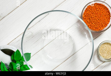 Glasplatten mit roten Linsen, Sesamsamen und eine große Glasplatte stehen auf einem weißen Tisch Stockfoto