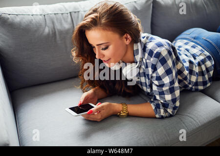 Porträt einer schönen Lächelnden jungen Frau liegt auf einem Sofa und zu Hause suchen, mit Bildschirm Stockfoto