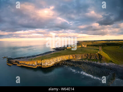 Ansicht aus der Luft zu den Embleton Meer, Nordsee, die Klippe mit Möwen, Ruinen und grüne Felder. Sonnenuntergang mit dramatischen Wolken. England Land Stockfoto