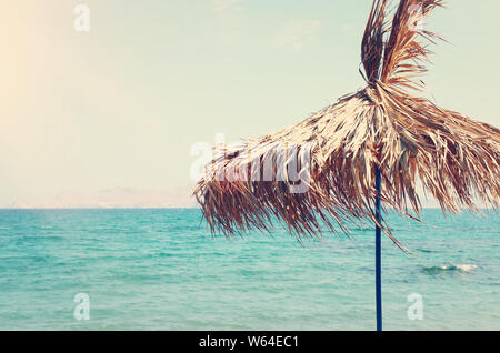 Urlaub Bild des tropischen Meeres und Sonnenschirm aus trockenen Palm Blätter gemacht. Sommer Reisen und Urlaub Konzept Stockfoto