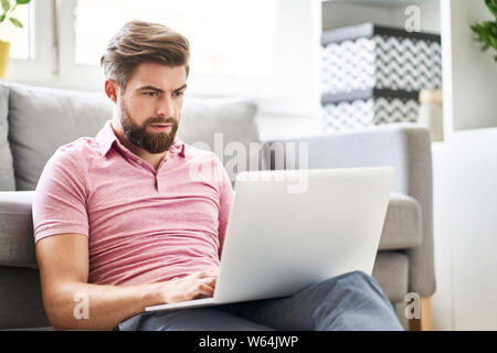 Betonte Mann mit Laptop zu Hause eingeben Nachricht Stockfoto