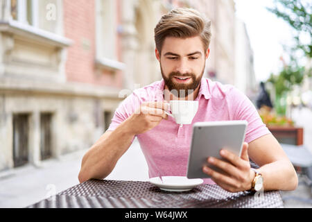 Junger Mann lesen Tablette im Freien Cafe, Kaffee zu trinken. Stockfoto