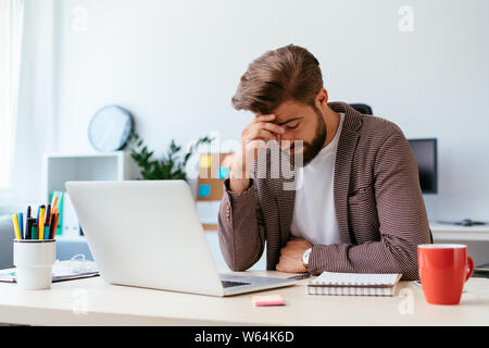 Junge Unternehmer am Schreibtisch sitzen und mit Kopfschmerzen während der Arbeit mit dem Laptop in modernen Büro Stockfoto