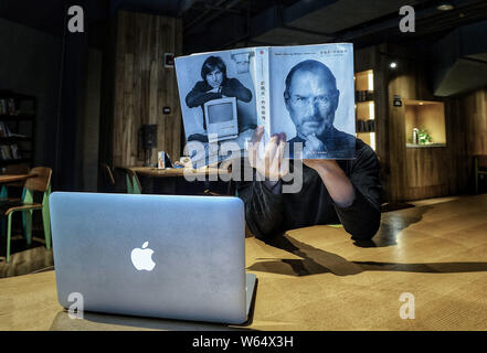 Ein Mitarbeiter von Chengdu Yan Ji Sie Buchhandlung stellt für eine erzwungene Perspektive Foto mit einem Buch mit dem Portrait von Apple Inc., Mitbegründer Steve Stockfoto