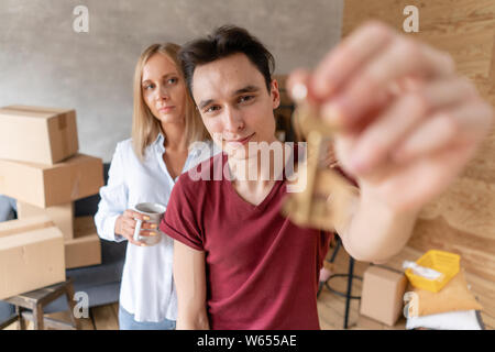 Junge glückliches Paar umarmen, zeigen Schlüssel zum neuen Haus. Glückliche Familie, Umzug in eine neue Wohnung zusammen. Umzug Konzept Stockfoto