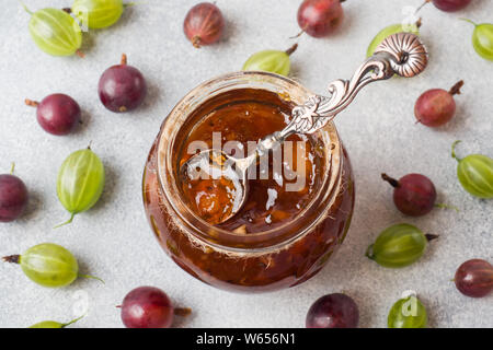 Gooseberry jam in einem Glas mit frischen Stachelbeeren Beeren auf grauem Hintergrund Stockfoto