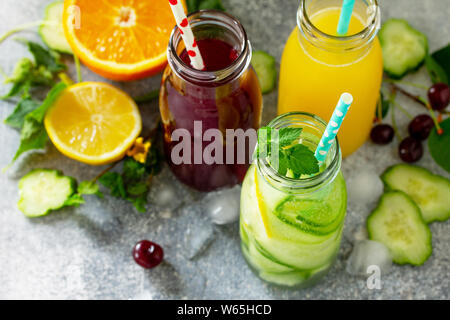 Verschiedene Erfrischungen Getränke - detox Gurken Wasser, Kirschsaft und Orangensaft auf Tisch aus Stein. Stockfoto