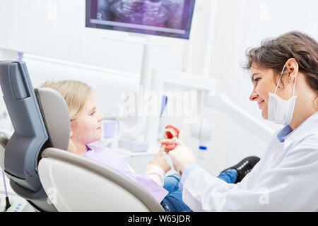 Freundliche ZFA oder Zahnarzt zeigt Kind als Patient einer Zahnprothese Modell und schafft Vertrauen Stockfoto